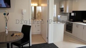 A modern kitchen with white cabinets, a microwave, and an oven. There is a dining area with a table and chairs, and a TV mounted on the wall. - Auckland Phoenix Palm (Auckland)