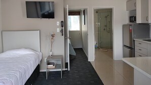 A hotel room with a bed, a TV, a small table with a vase, a kitchenette, and a shower area. - Auckland Phoenix Palm (Auckland)