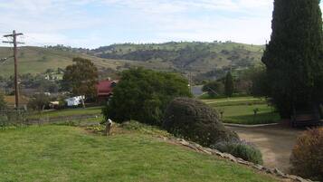 Paisaje rural con colinas onduladas, una casa de techo rojo y un alto ciprés.