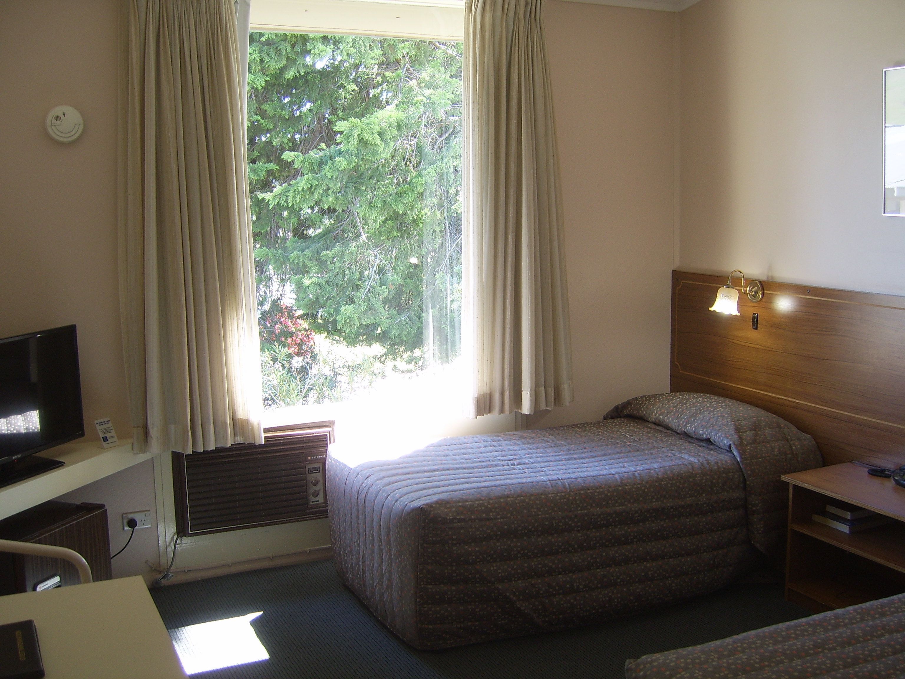 Habitación de hotel con cama, escritorio con televisor, mesita de noche y ventana con cortinas.