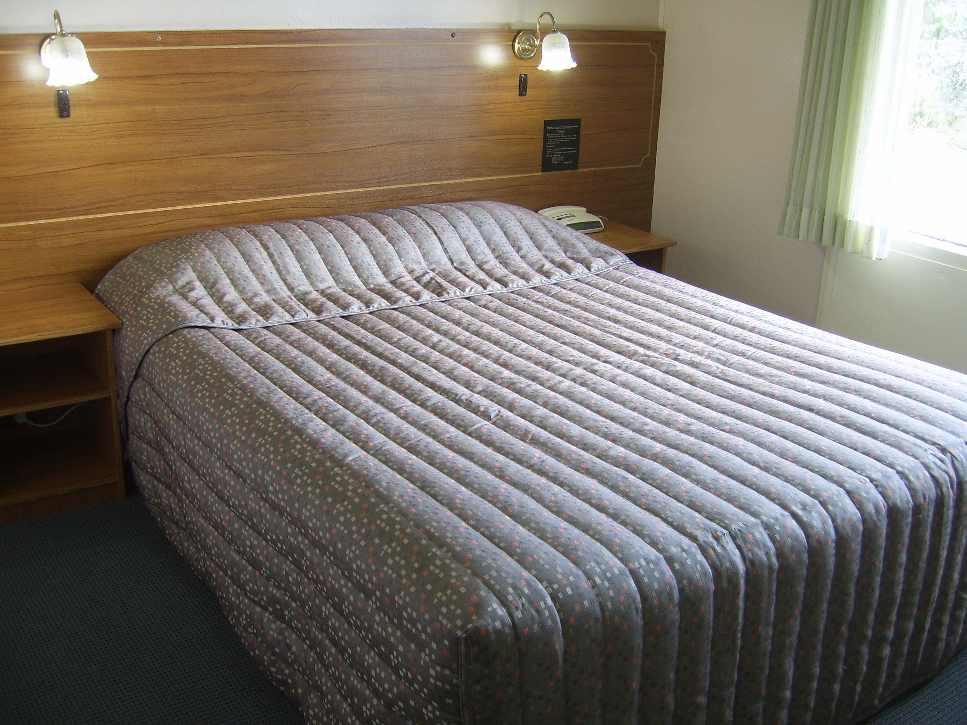 A neatly made bed with a patterned bedspread, a wooden headboard, bedside lamps, and a bedside phone.