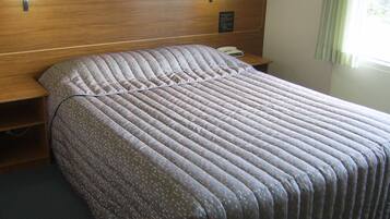 A neatly made bed with a patterned bedspread, a wooden headboard, bedside lamps, and a bedside phone.