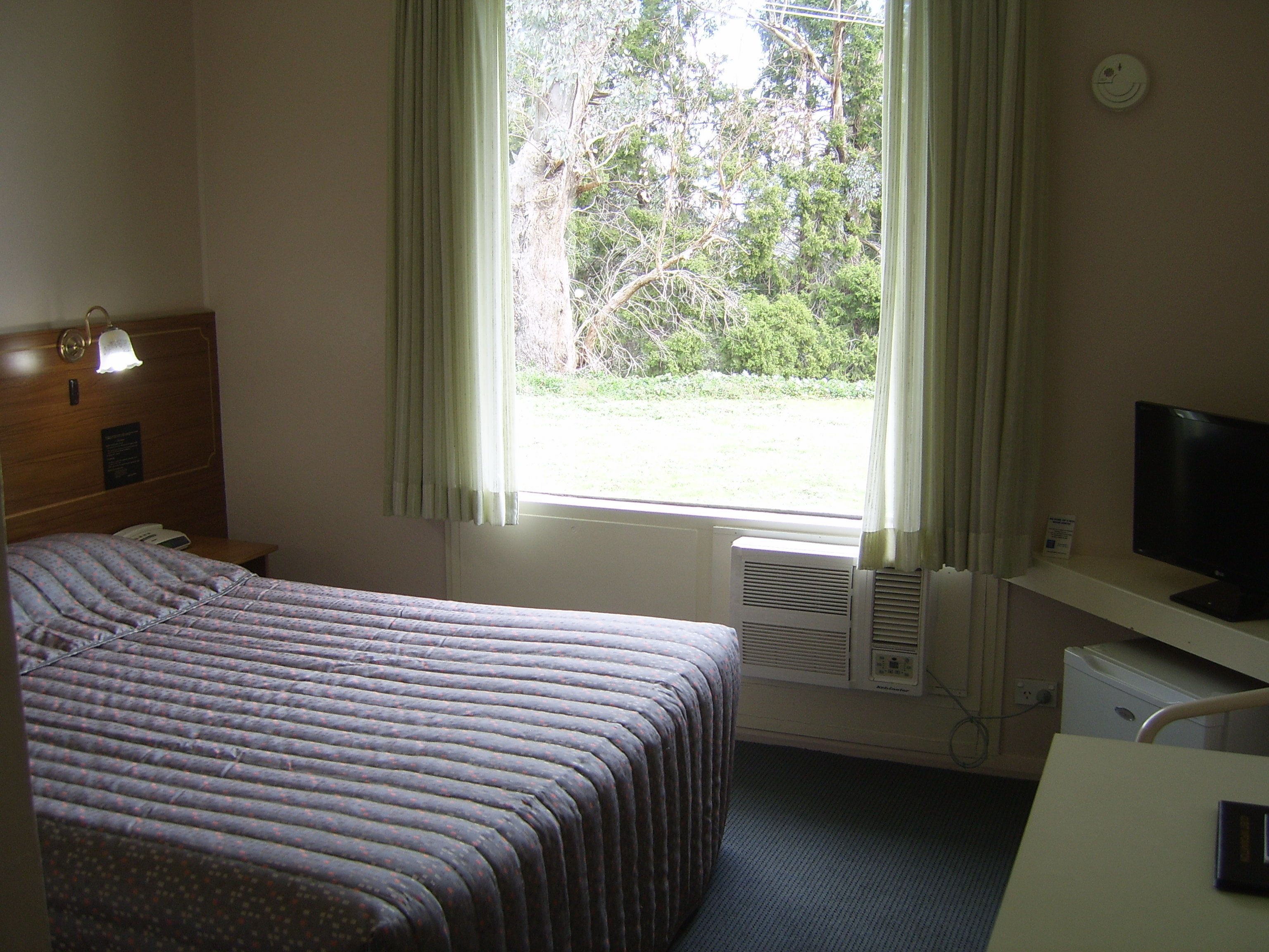 Une chambre d’hôtel avec un lit, un bureau équipé d’un ordinateur, une fenêtre avec des rideaux et une horloge fixée au mur.