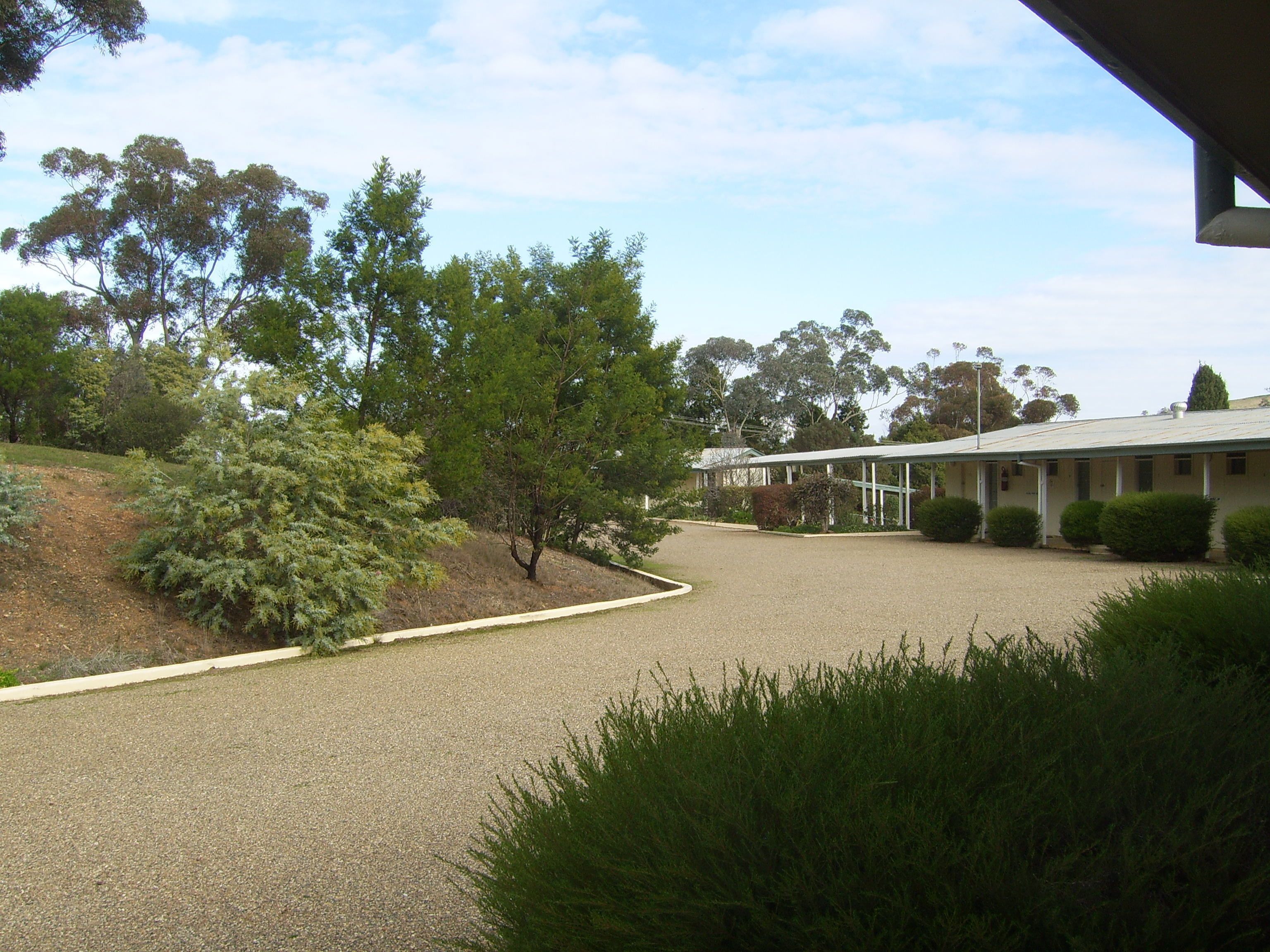 A building with a covered outdoor area, surrounded by trees and shrubs.