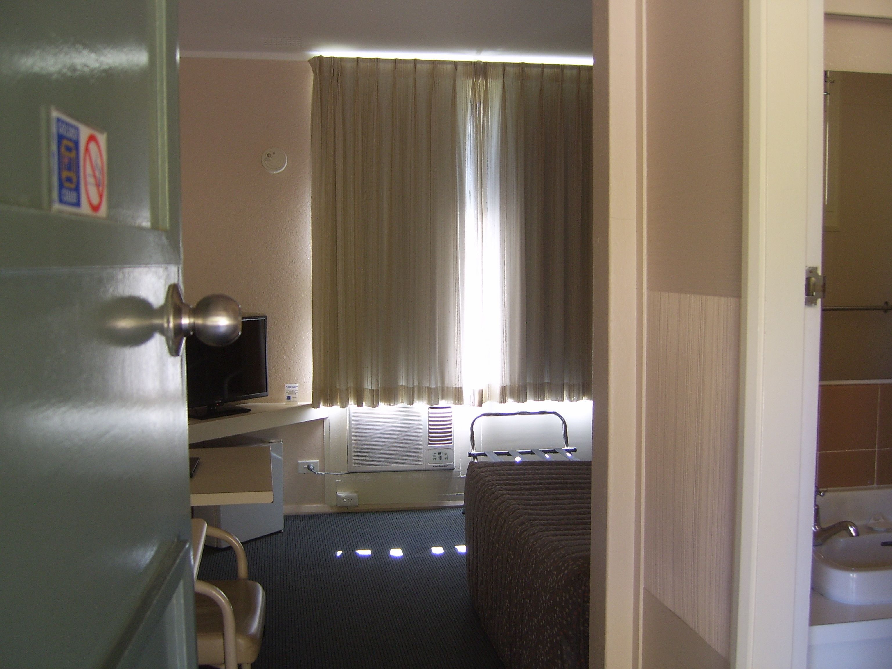 Una habitación de hotel con cama, escritorio con computadora, televisor y ventana con cortinas.