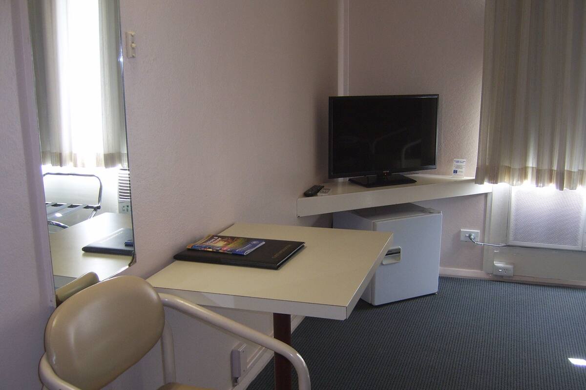 A hotel room with a bed, a desk with a chair, a television, and a small refrigerator.
