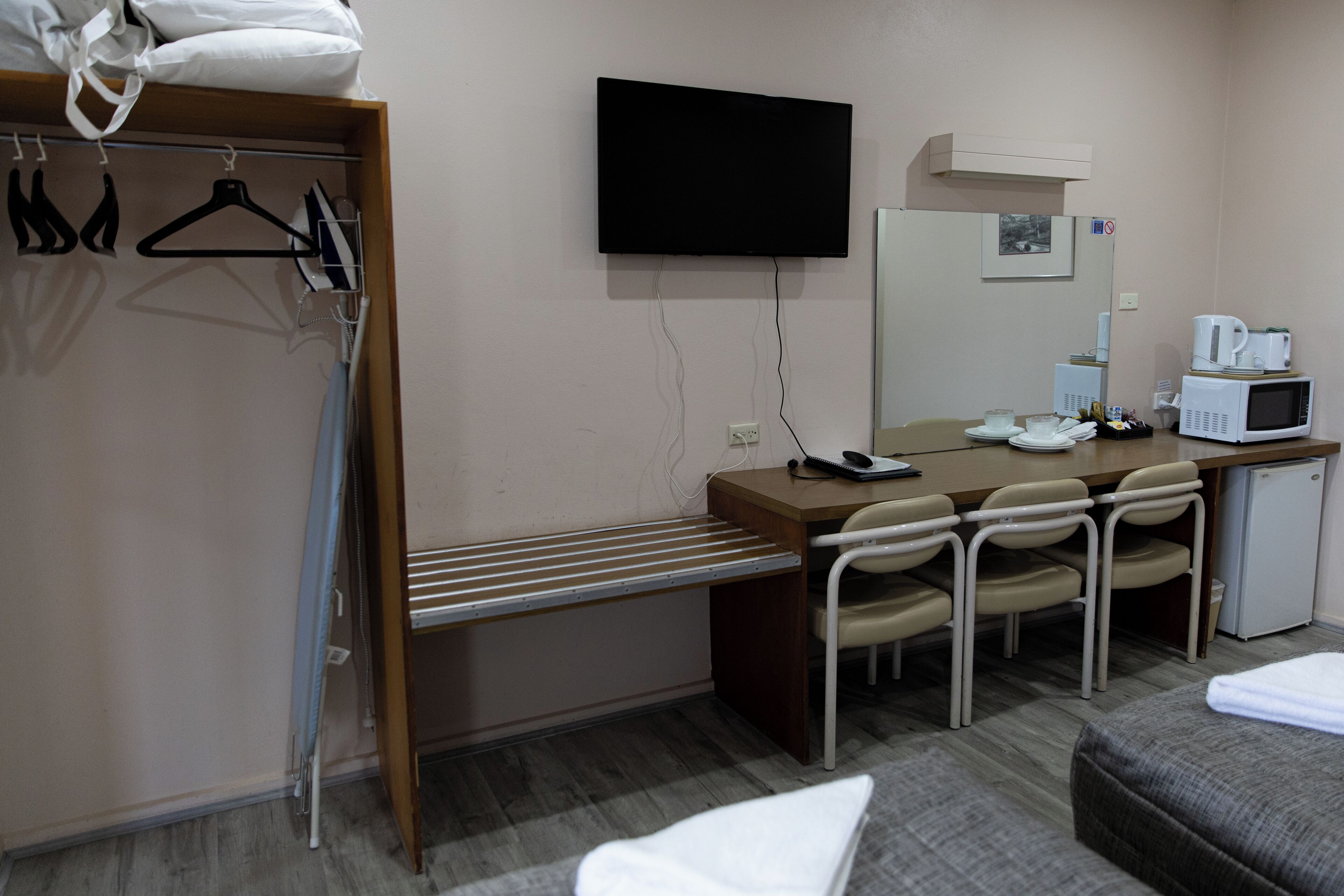 Habitación de hotel con cama, escritorio con silla, televisor, microondas y refrigerador pequeño.