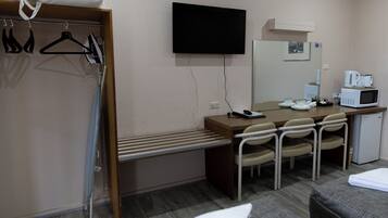 Habitación de hotel con cama, escritorio con silla, televisor, microondas y refrigerador pequeño.