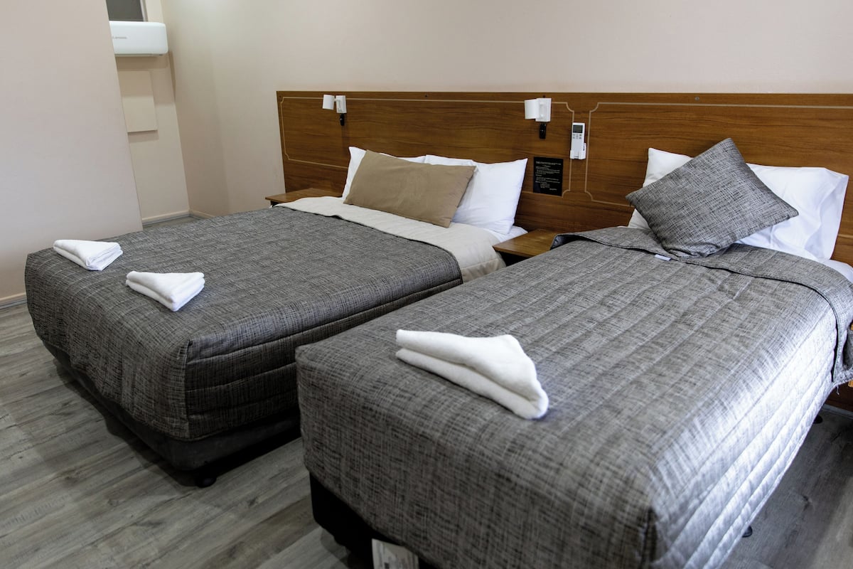 Two twin beds with grey bedding and white towels, wooden headboards, and a wooden floor.