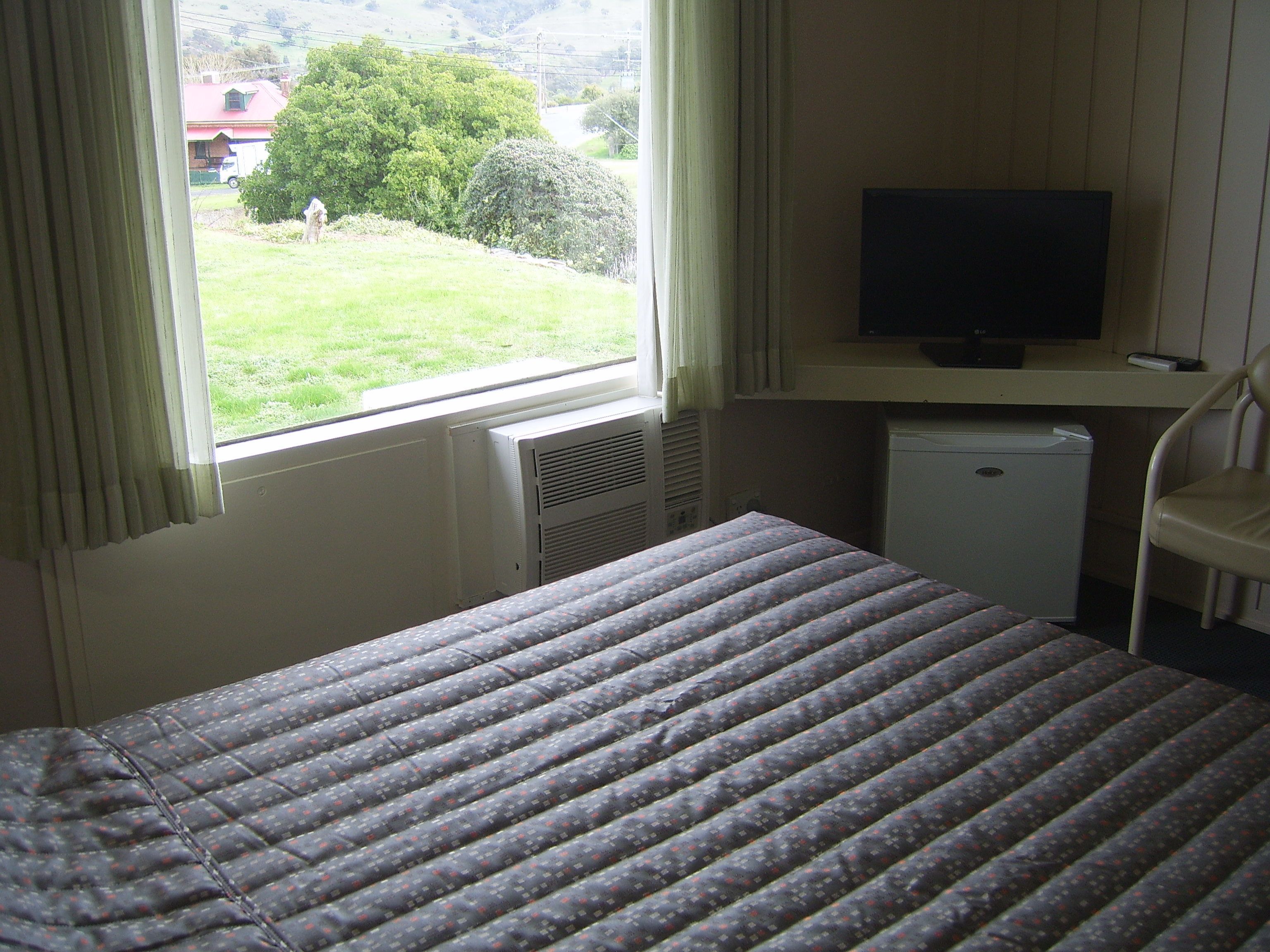 Una habitación con una cama, televisor, un electrodoméstico pequeño y una ventana con cortinas.