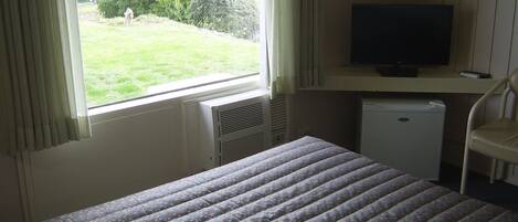 Una habitación con una cama, televisor, un electrodoméstico pequeño y una ventana con cortinas.