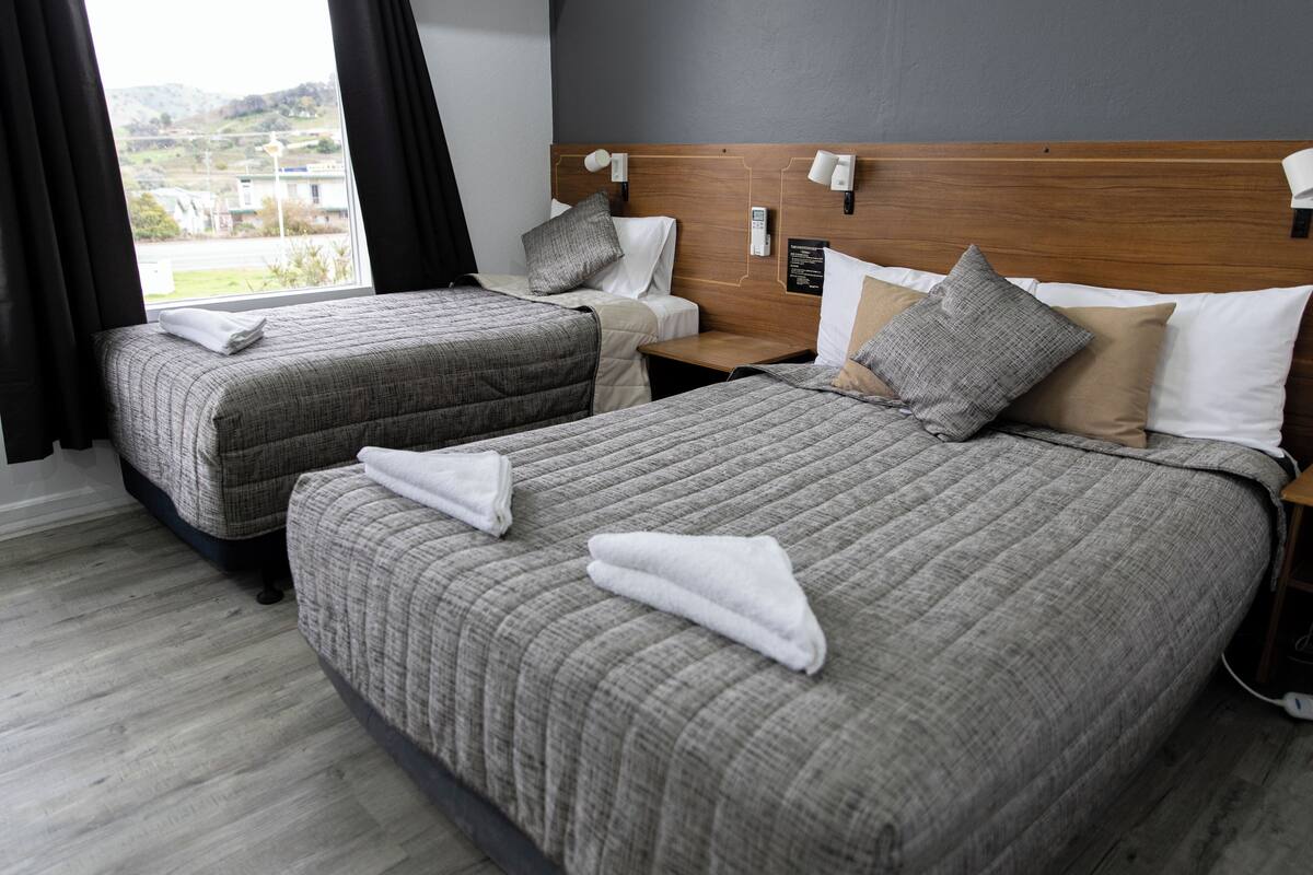A hotel room with two beds, a wooden headboard, bedside lamps, and a view of the outdoors.