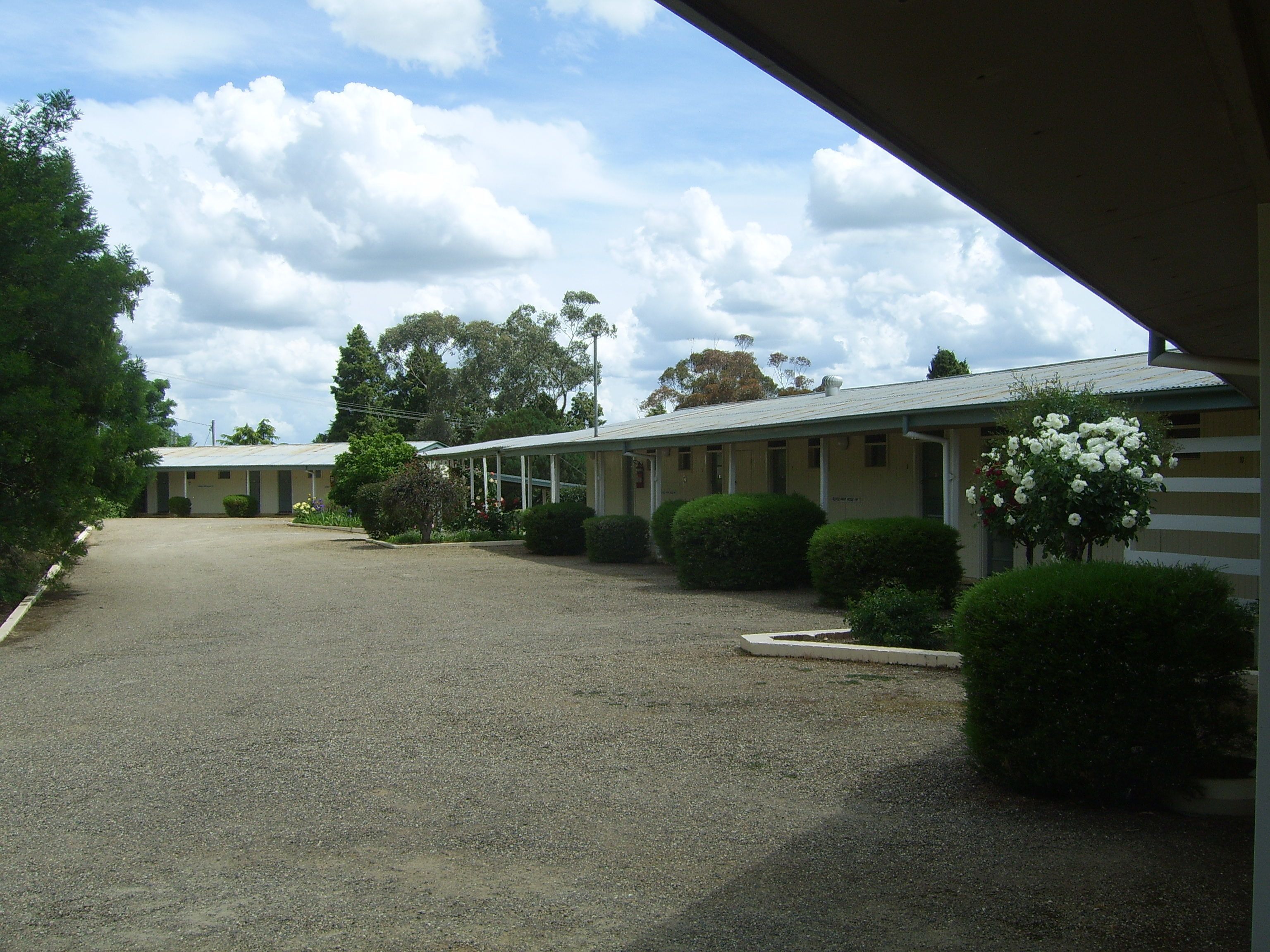 A motel with a gravel driveway, covered parking, and neatly trimmed bushes.