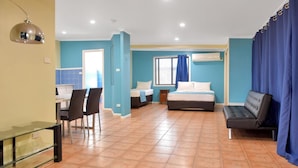 A room with a bed, a sofa, a dining table with chairs, and a small table with a lamp. - Adobe Motel (Cairns North)