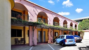 A building with pink arches and yellow walls, featuring a parking area with two cars. - Adobe Motel (Cairns North)