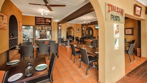 A restaurant with tables and chairs, a ceiling fan, and a sign for Italian pasta. - Adobe Motel (Cairns North)