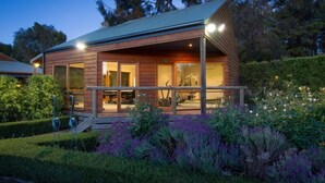A modern wooden cabin with a covered porch, large windows, and a well-maintained garden with purple flowers. - Glen Erin At Lancefield - Vineyard Retreat (Lancefield)