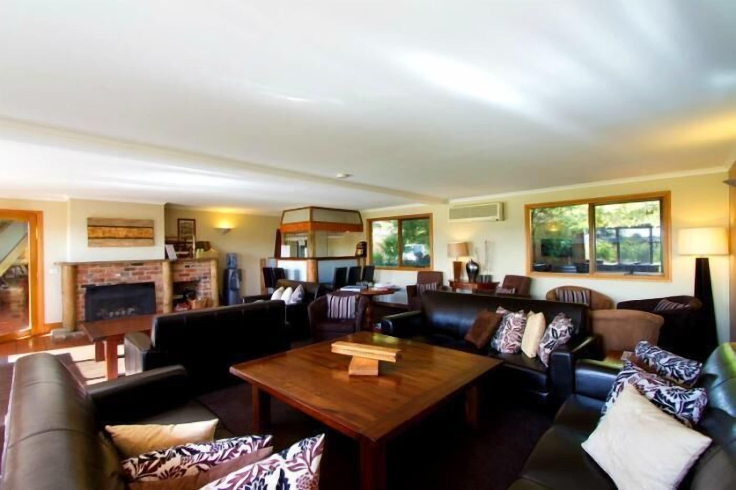 A spacious living room with a fireplace, leather sofas, a wooden coffee table, and large windows offering a view of the outdoors.