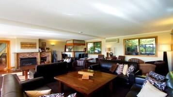 A spacious living room with a fireplace, leather sofas, a wooden coffee table, and large windows offering a view of the outdoors.
