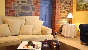 Una habitación acogedora con una pared de piedra, una puerta azul, un sofá color beige, una pequeña mesa con una botella y vasos, y un cuadro en la pared.