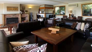 A spacious living room with a fireplace, leather sofas, a wooden coffee table, and a large window offering a view of greenery.