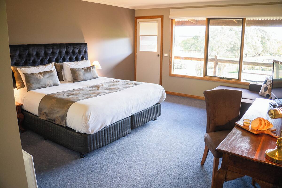 A bedroom with a large bed, a desk with a chair, and a window with a view of trees.