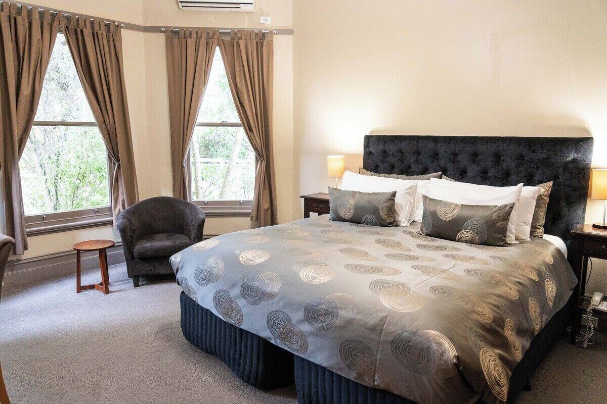A bedroom with a large bed, two bedside tables, a chair, and a window with curtains.