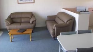 A room with two brown sofas, a wooden coffee table, a white table, and a framed picture on the wall.