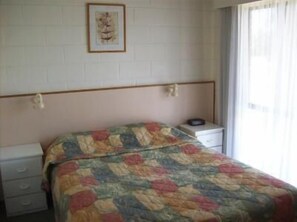 A bedroom with a bed, a nightstand, a framed picture on the wall, and a window with curtains. - Black Swan Motor Inn (Lakes Entrance)
