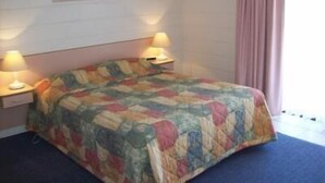 A hotel room with a bed, two bedside lamps, a framed picture on the wall, and a window with curtains.