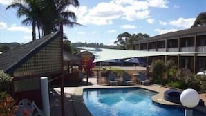 A pool area with a pool, lounge chairs, and a building with a sloped roof.