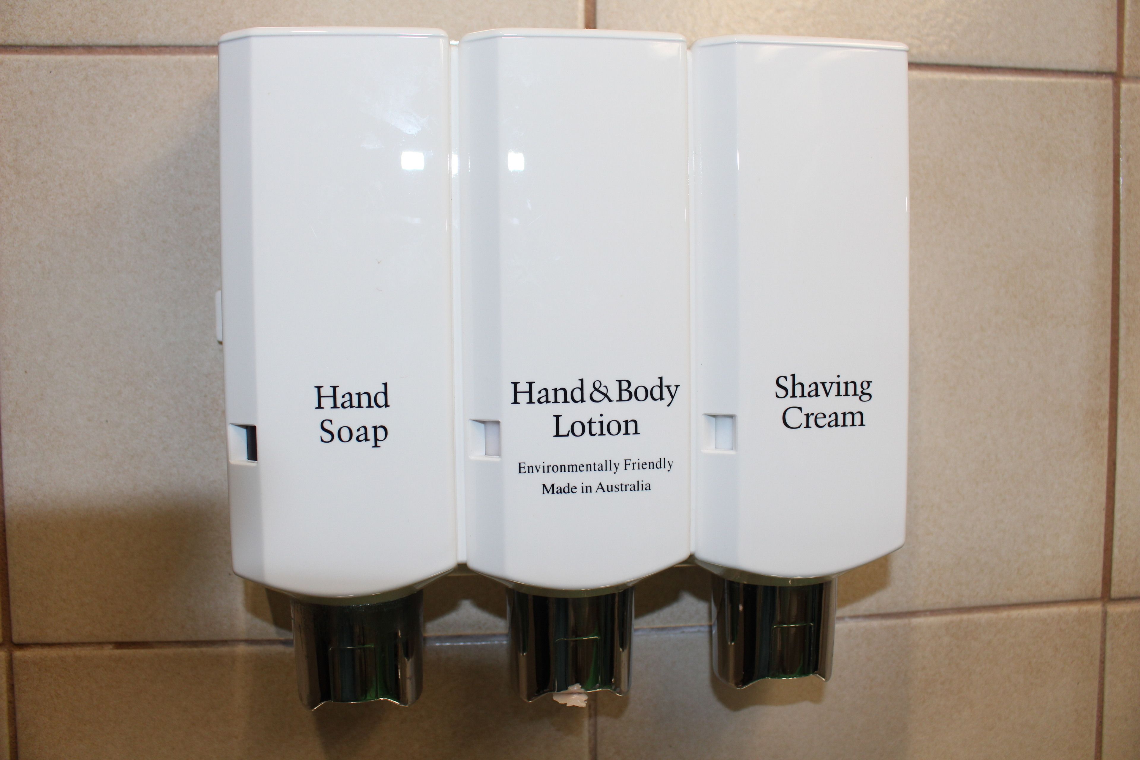 Three dispensers labeled "Hand Soap," "Hand & Body Lotion," and "Shaving Cream" in a restroom.
