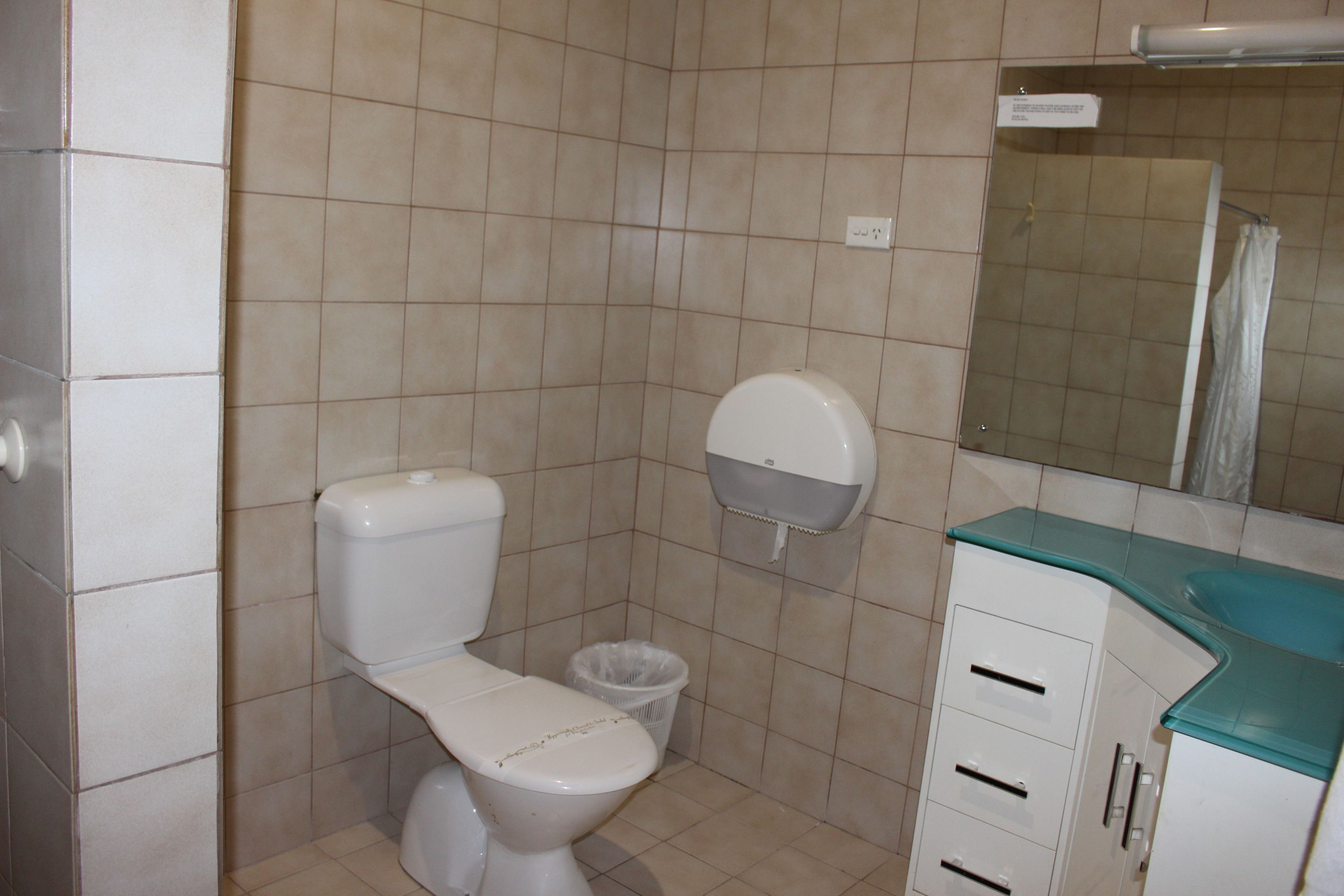A bathroom with a toilet, a trash bin, a sink with a mirror, and a cabinet.