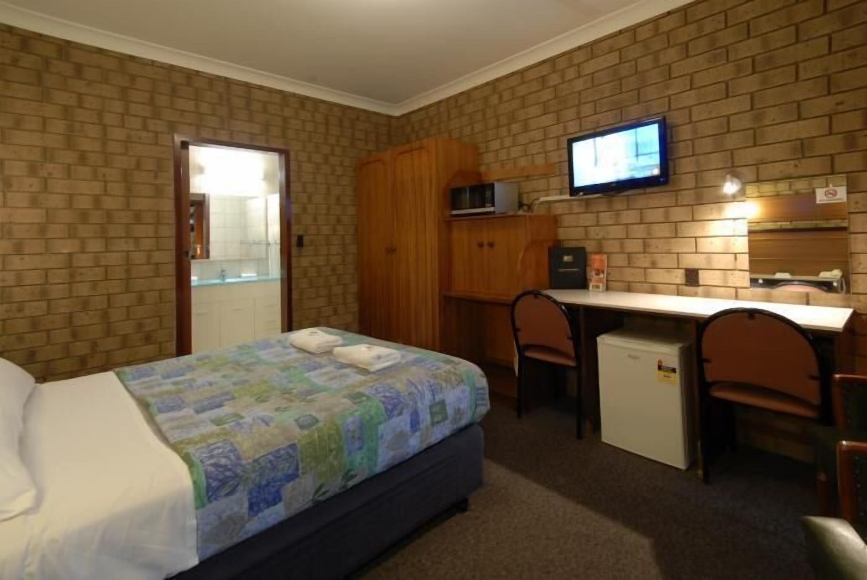 A hotel room with a bed, a desk, a chair, a television, and a small refrigerator.