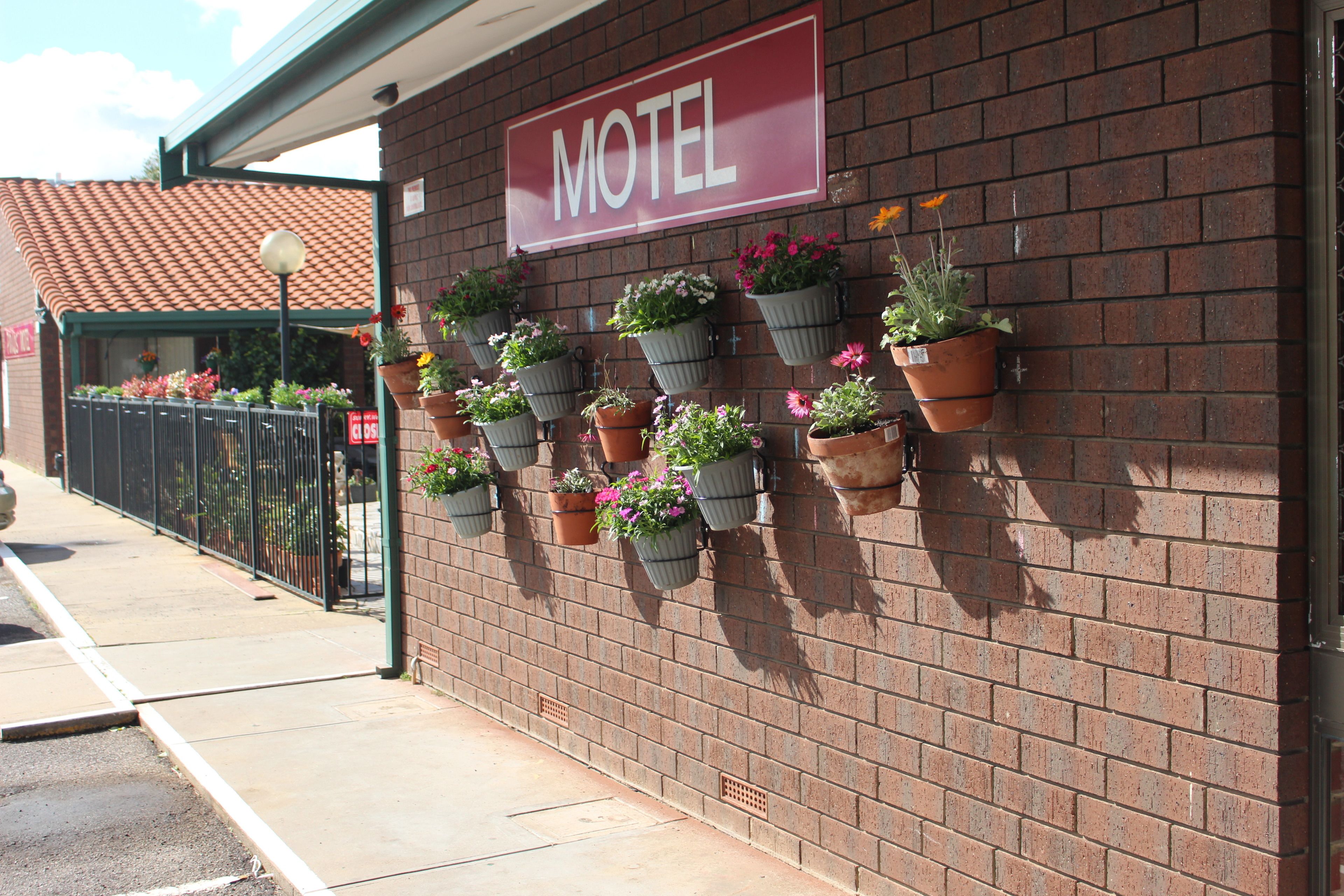 A motel with a red sign, brick exterior, and multiple flower planters on the wall.