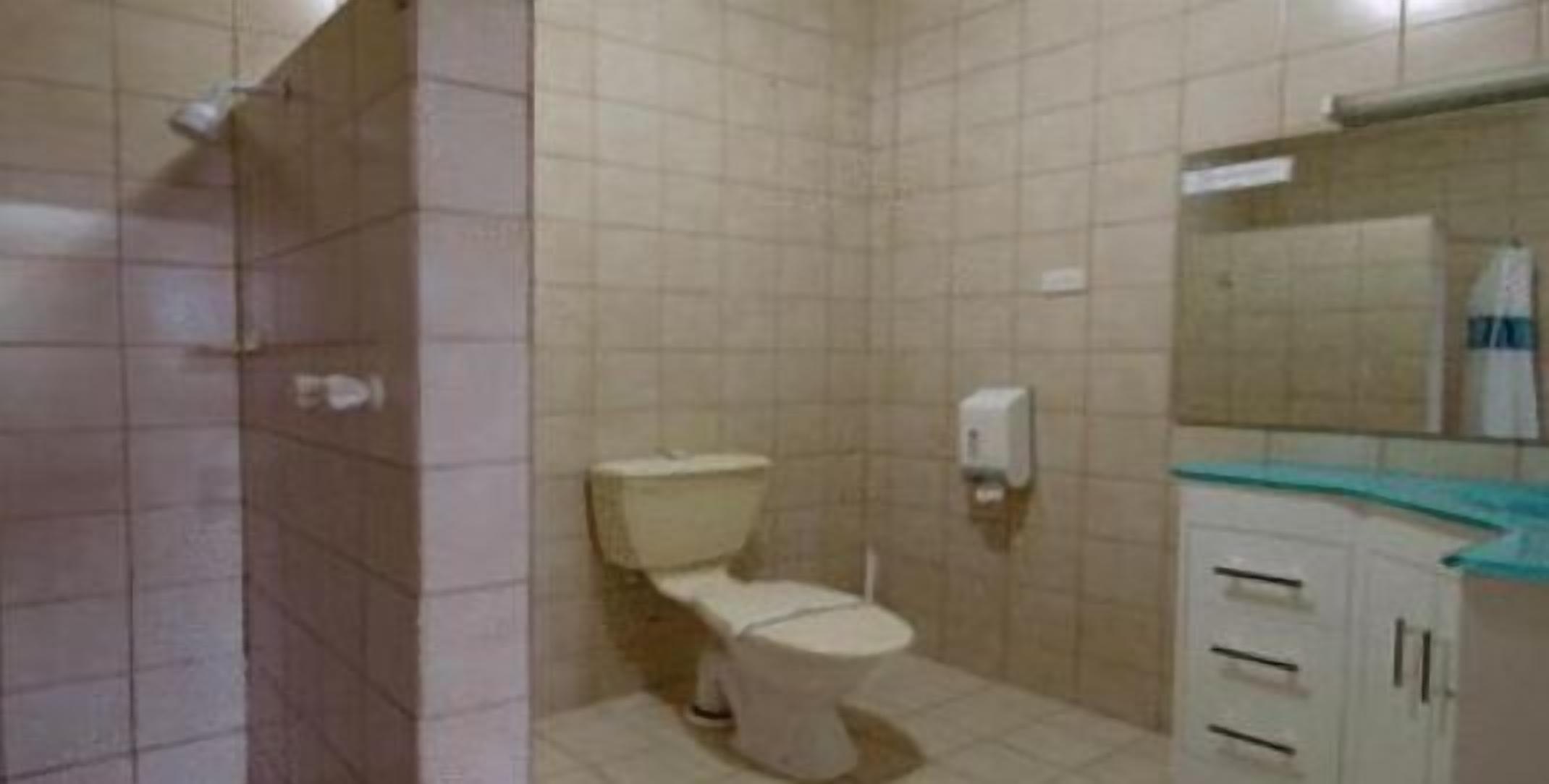 A small, tiled bathroom with a toilet, a hand dryer, and a mirror above a sink.