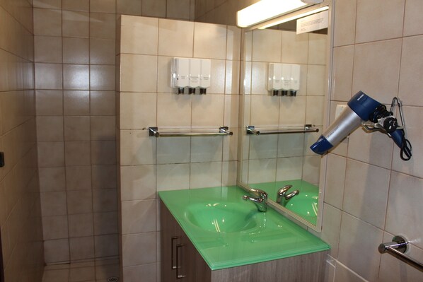 Un baño con un lavamanos verde, un espejo y un secador de pelo fijado en la pared.