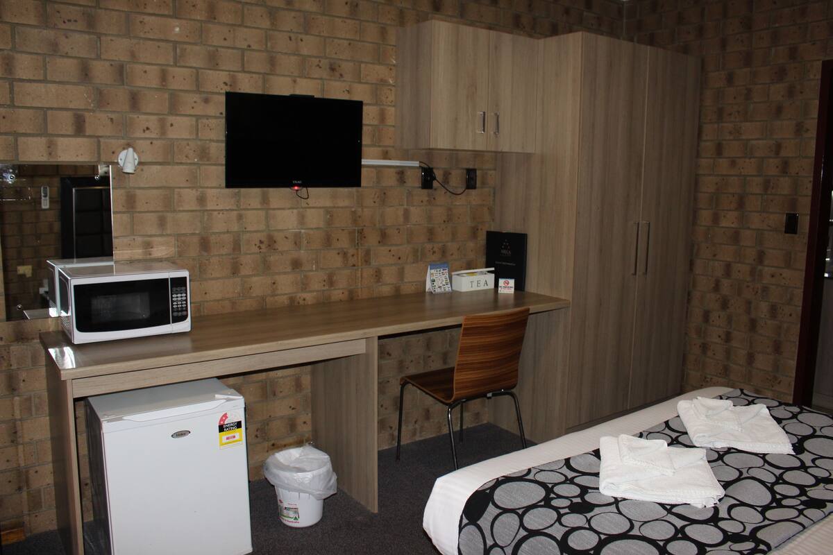 Una habitación de hotel compacta con kitchenette, una cama con toallas, un televisor y un armario de madera.