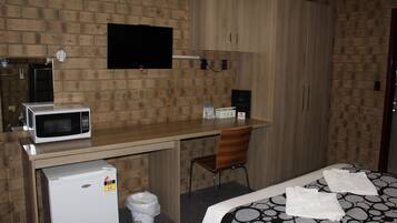 Una habitación de hotel compacta con kitchenette, una cama con toallas, un televisor y un armario de madera.