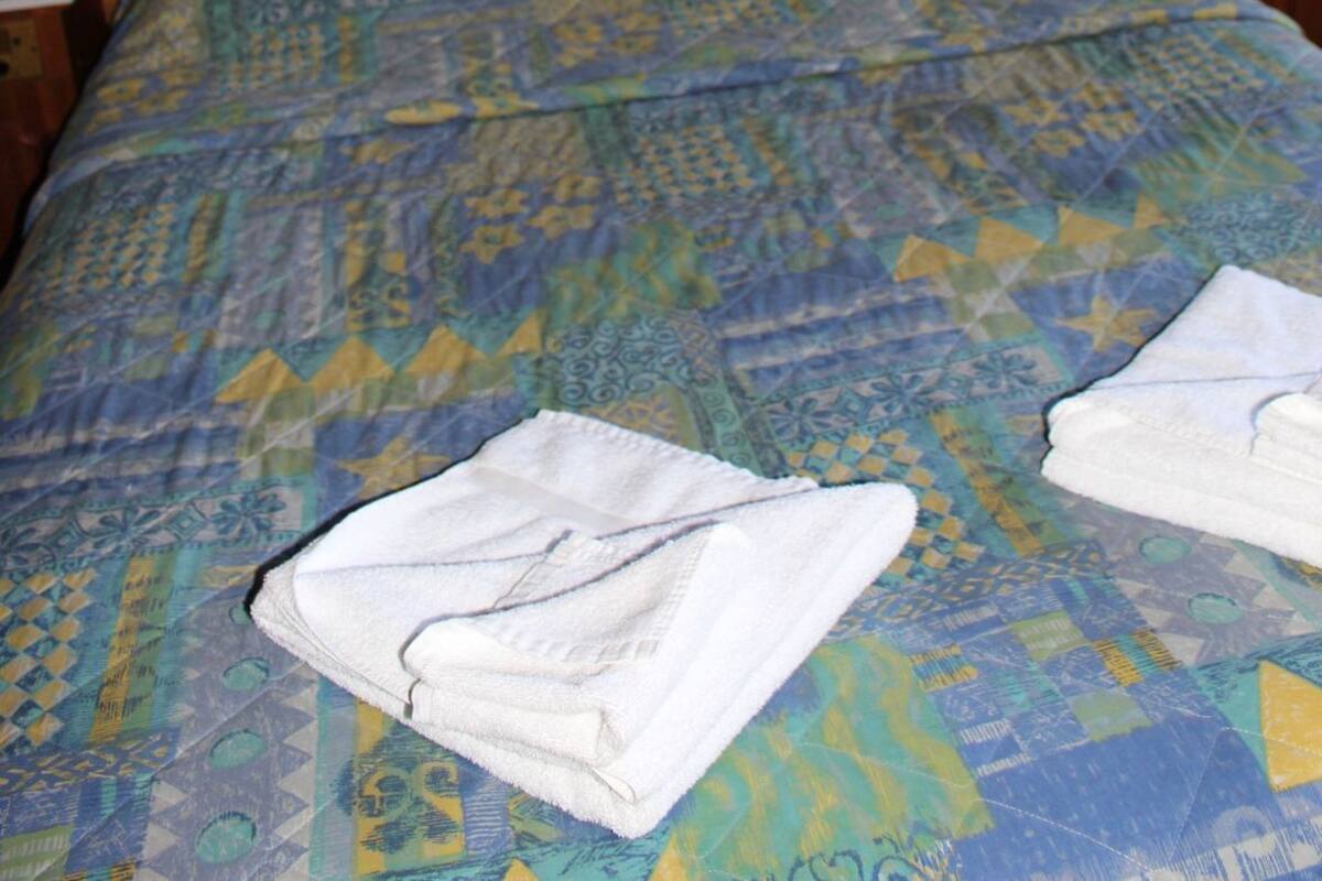 Una cama con una colcha estampada, un cabecero de madera, una mesita de noche con una lámpara y un cuadro enmarcado en la pared.