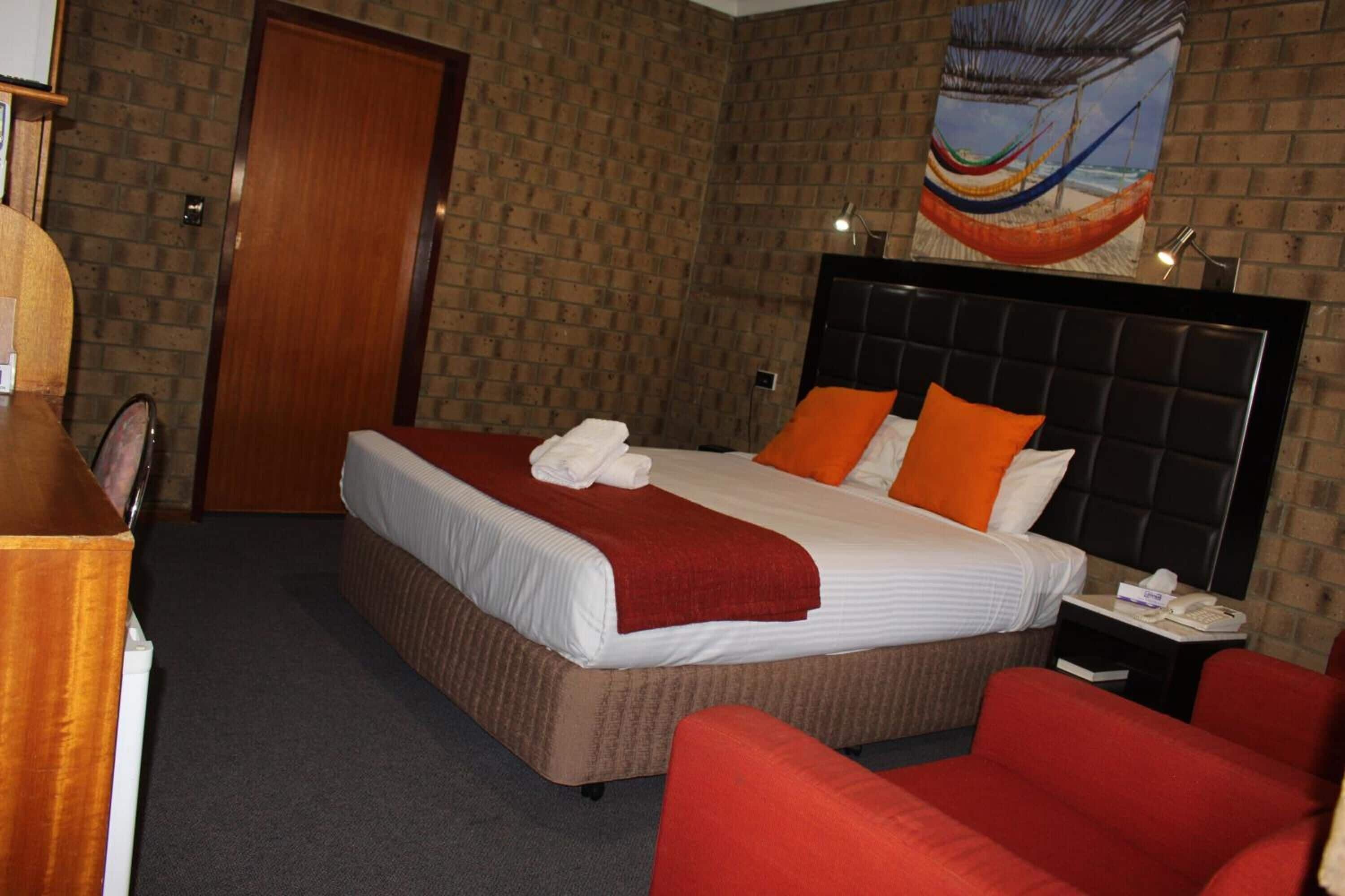 A hotel room with a large bed, a wooden door, a painting on the wall, and a red chair.