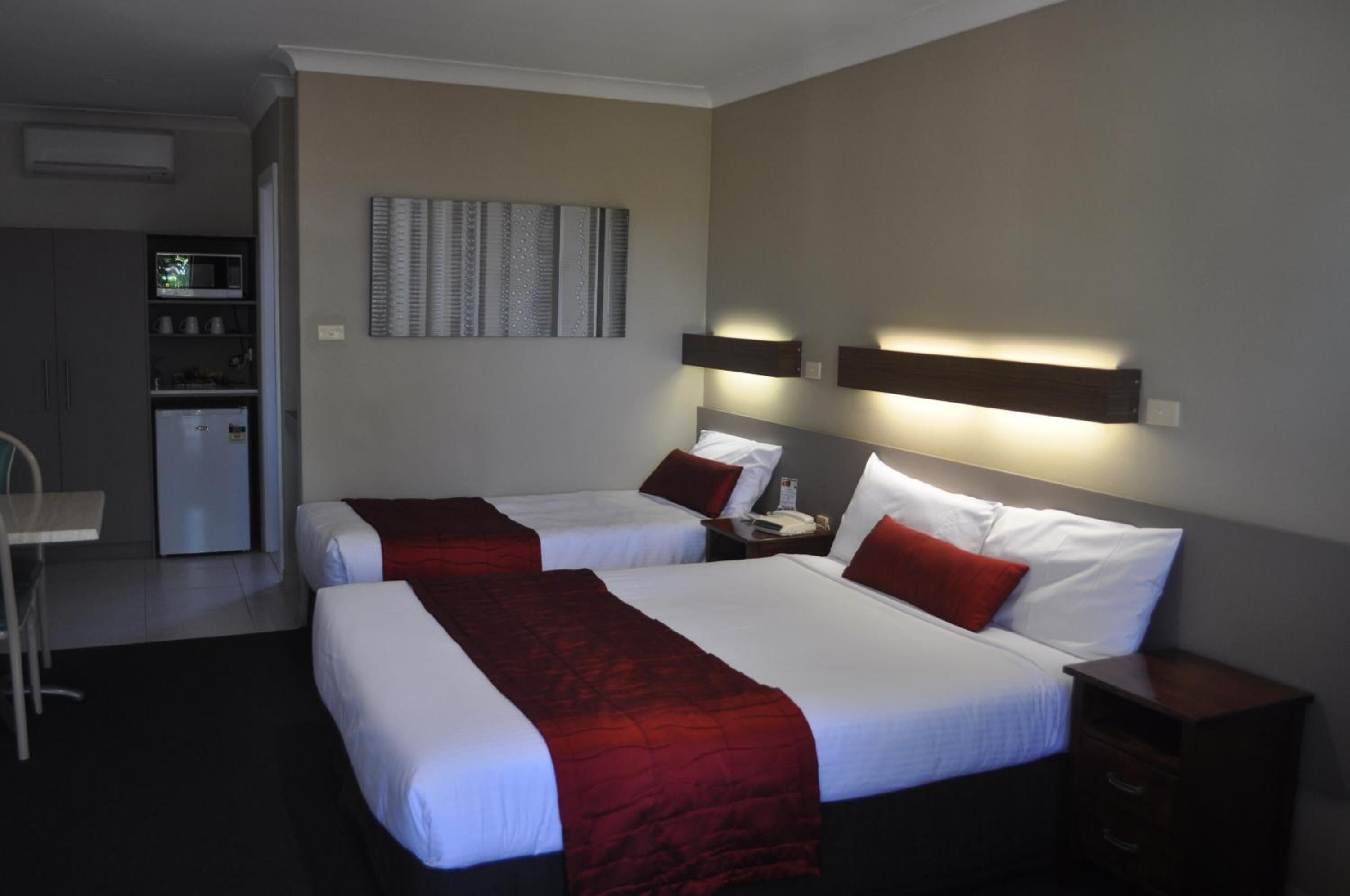 A hotel room with two beds, a desk, a microwave, and a refrigerator.