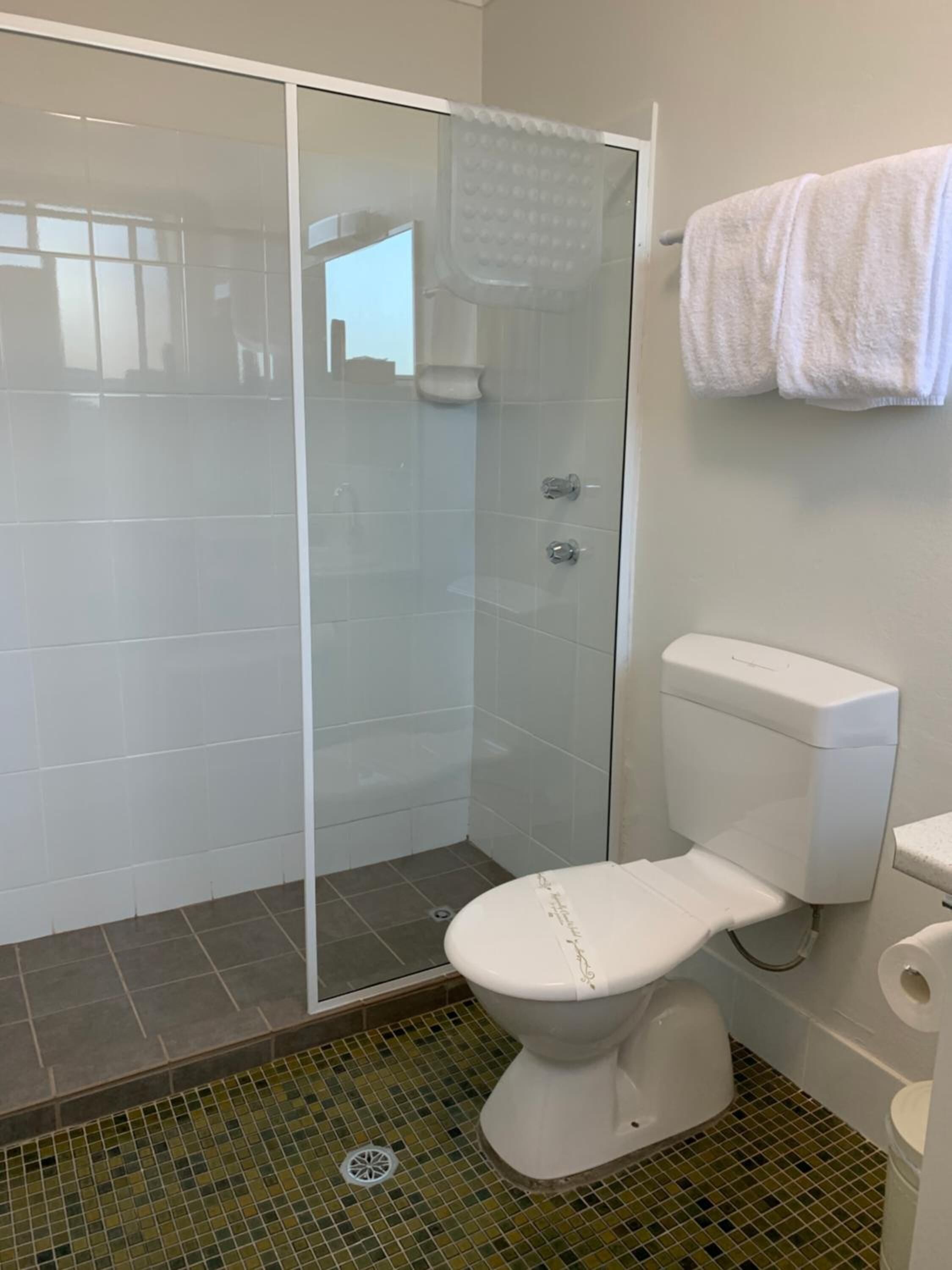Une salle de bain moderne avec une douche à parois de verre, des toilettes et un sol carrelé.
