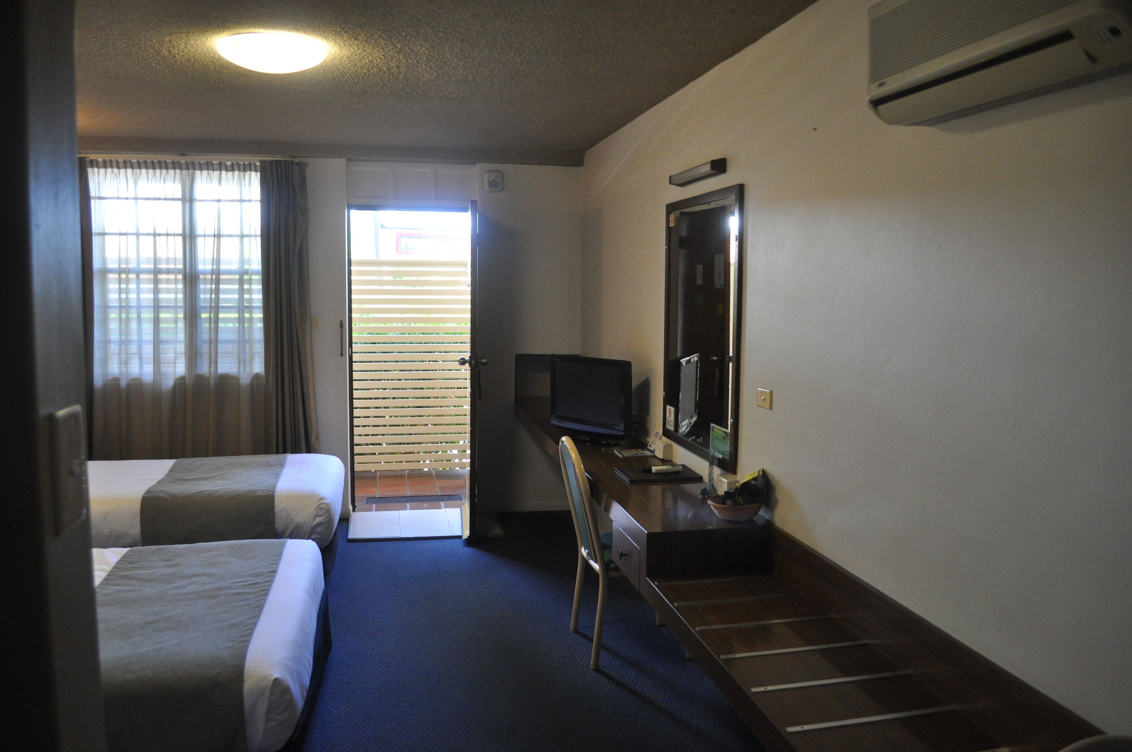 A hotel room with two beds, a desk with a computer, a television, and a large mirror.