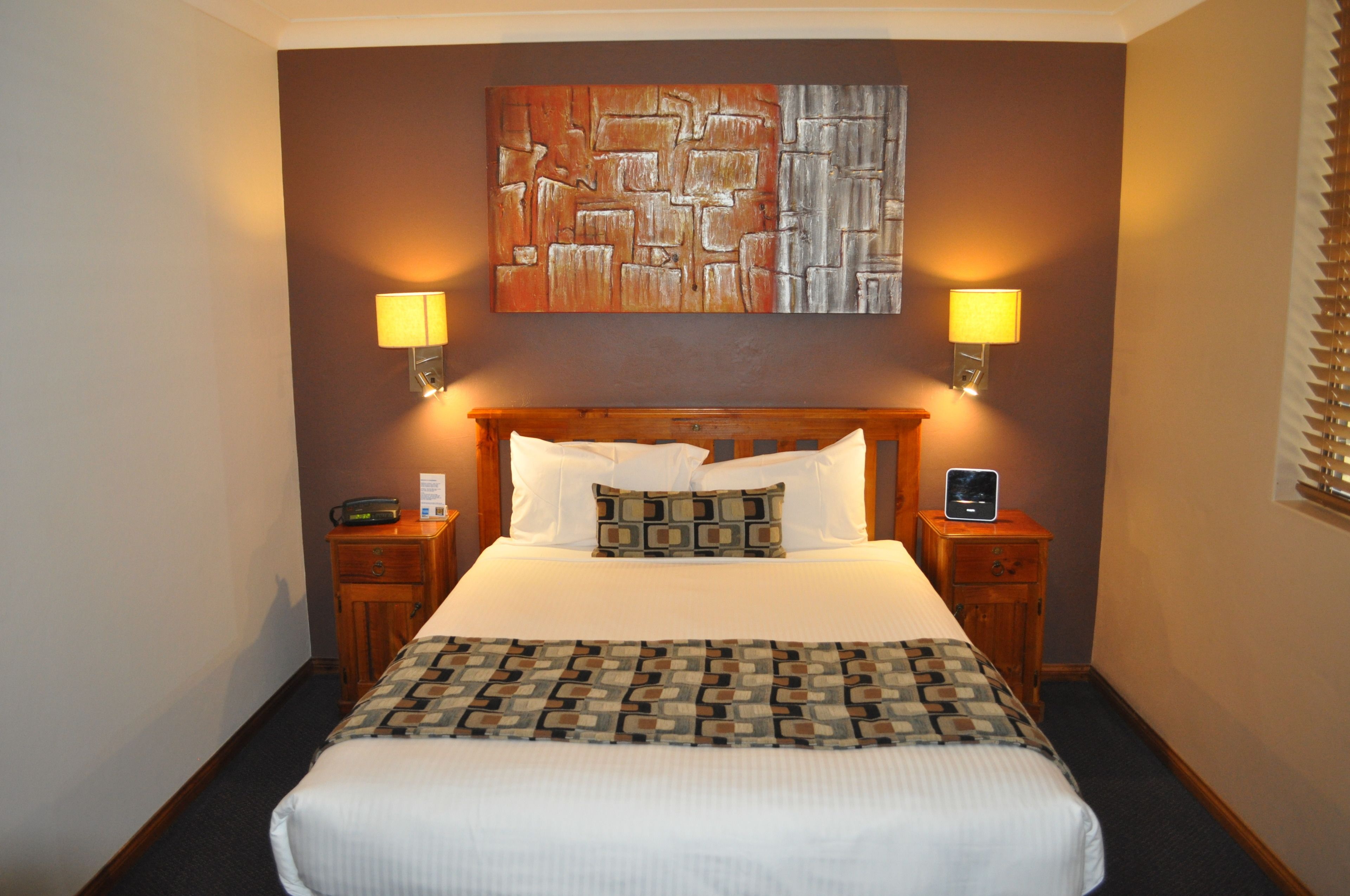 Habitación de hotel con una cama grande, dos mesitas de noche, una lámpara de noche y una obra de arte colgada en la pared, además de dos lámparas de pared.