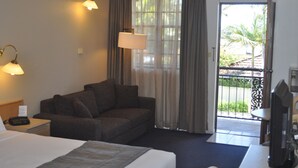 A hotel room with a bed, a sofa, a desk, a television, and a balcony with curtains. - In Town Motor Inn (Taree)