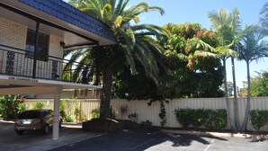 A building with a tiled roof, a covered parking area, and a white fence. - In Town Motor Inn (Taree)