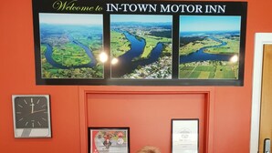 A reception desk at IN-TOWN MOTOR INN with a framed welcome sign, a clock, and two framed certificates. - In Town Motor Inn (Taree)