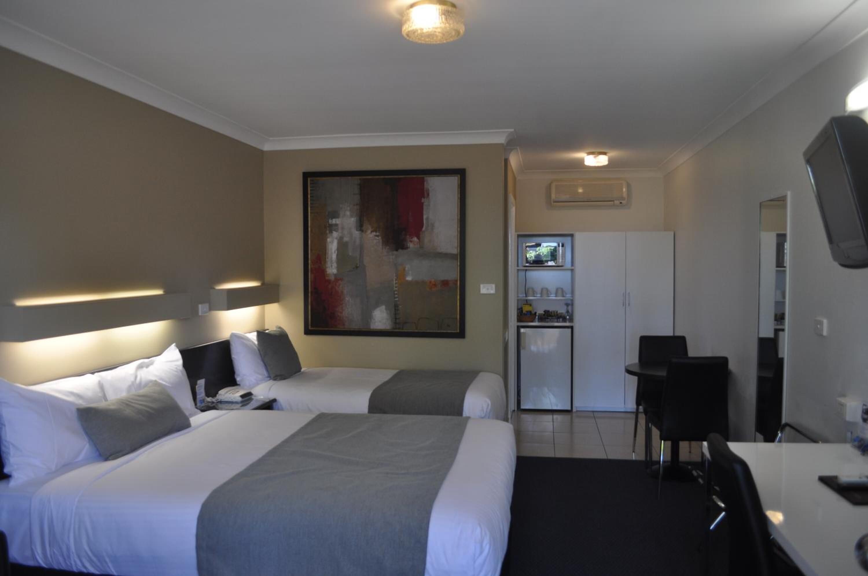 A hotel room with two beds, a desk, a chair, a television, and a refrigerator.