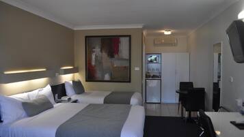 A hotel room with two beds, a desk, a chair, a television, and a refrigerator.